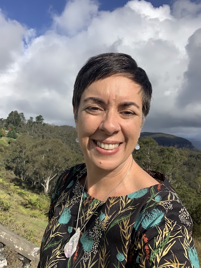 woman with short hair looks at camera with a treed background